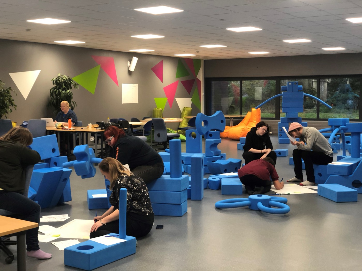 Adults building a pop-up playground from large blue foam blocks at a Build & Play Academy session
